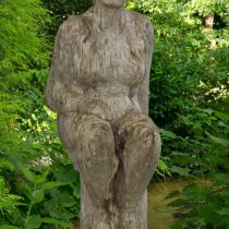 Eine Holzskulptur, die eine sitzende Frau darstellt.
