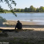 Am Rodenkirchener Rheinufer sitzt ein Mann mit dem Rücken zum Fotografen